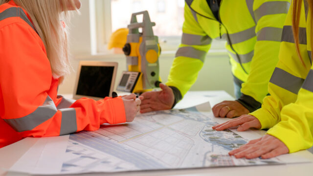A group of engineers in high-vis workwear review a site plan 