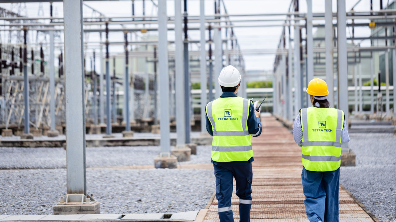 Image of two people walking through a building site wearing high visibility vests with the Tetra Tech logo on the back