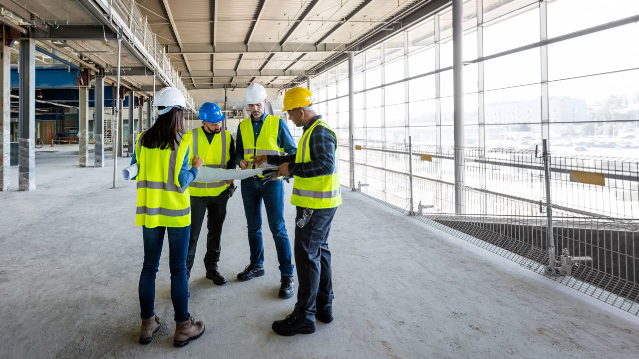 group of workers in high vis vests and hard hats look at building plan blueprint