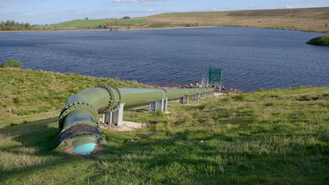 green pipe feeding water into a deep blue rural reservoir in the United Kingdom