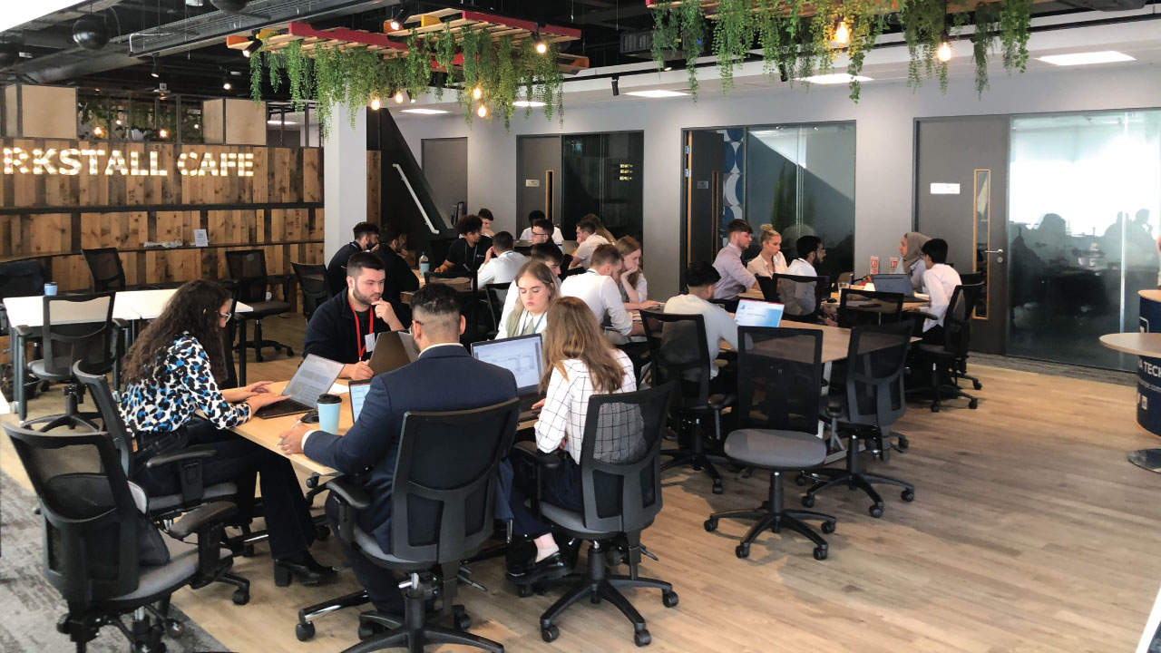 View of a large open space in an office setting with people sitting in desk chairs around several tables