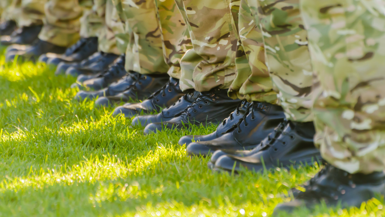 Closeup image of a line of people standing in a line on the grass, photo showing only shoes and camouflage trousers