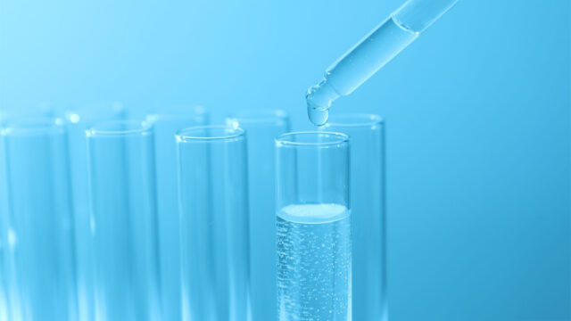 Closeup view of a pipette dropping clear liquid into a test tube