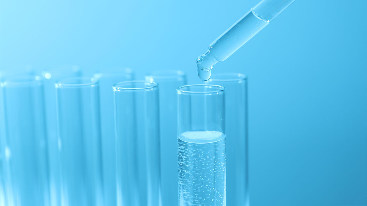 Closeup view of a pipette dropping clear liquid into a test tube