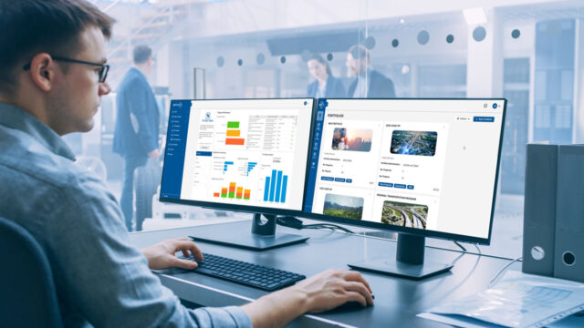 A person sitting at a desk looking at two computer monitors displaying myProjects dashboards