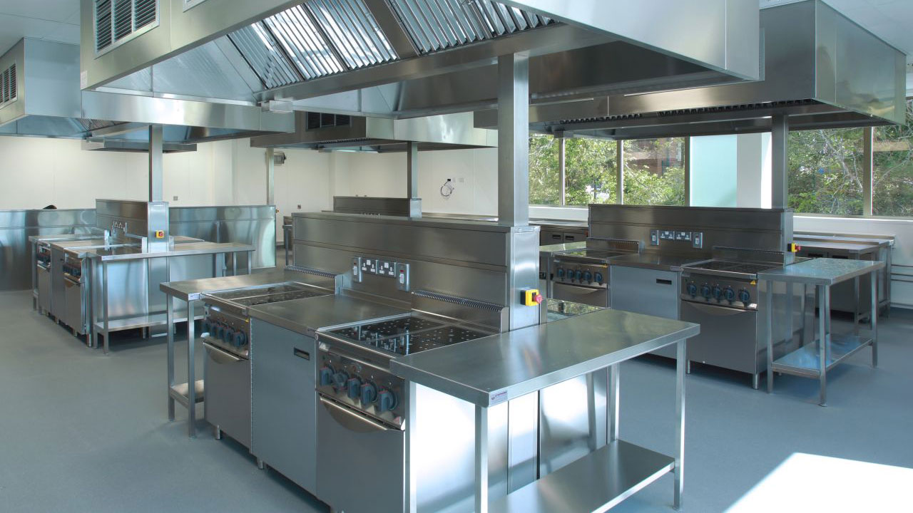 A modern commercial kitchen with stainless steel appliances, including stovetops and ventilation hoods