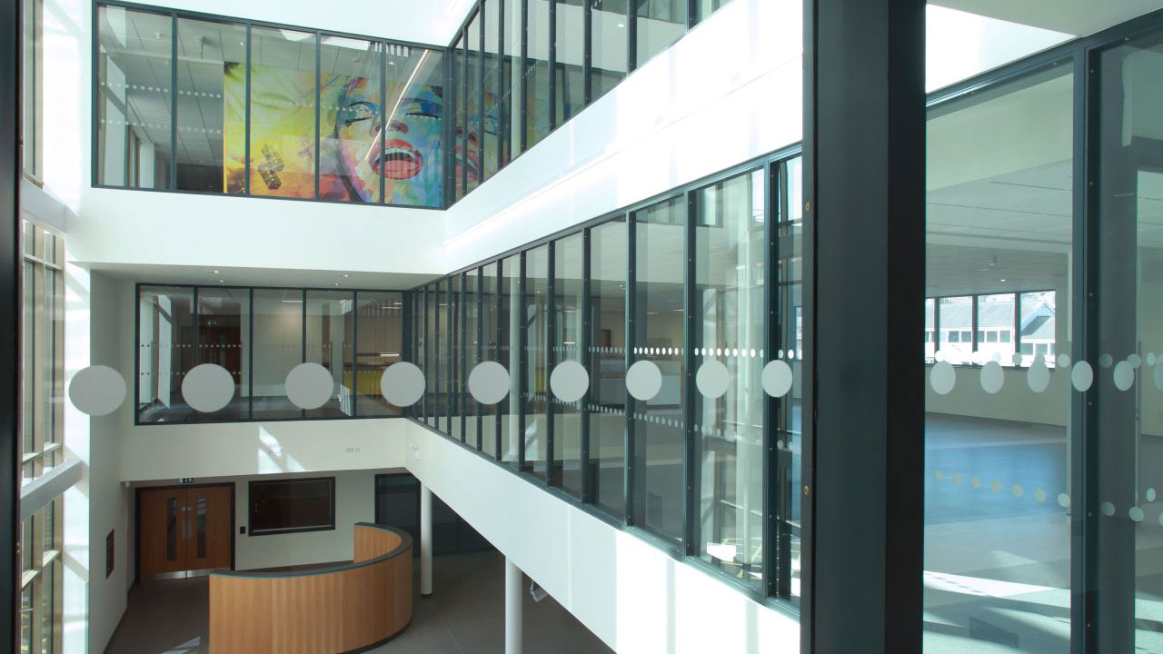 Interior view of a modern building atrium featuring glass walls, colorful artwork, and circular design elements