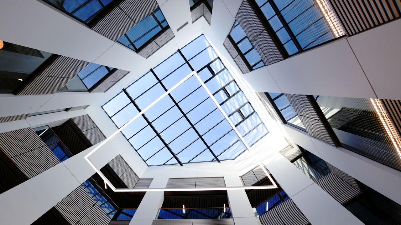A modern atrium with a glass ceiling and geometric lighting, viewed from below.
