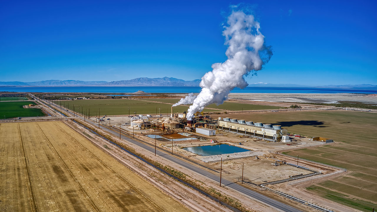 View of a geothermal plant with steam coming out of the stack rising into a blue sky