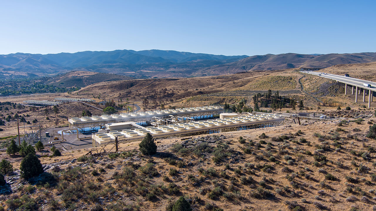 Desert fields with mountains in the background and geothermal storage facilities in the foreground