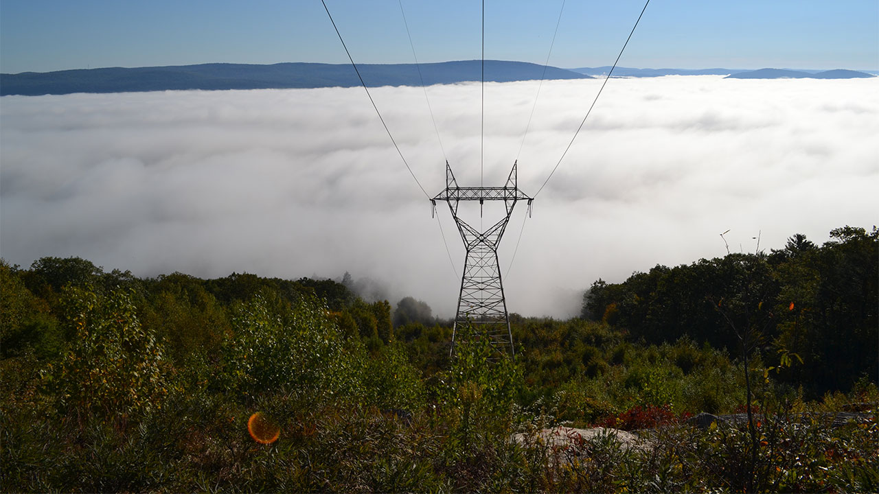 Power lines running downhill with a cloudy sky in the background
