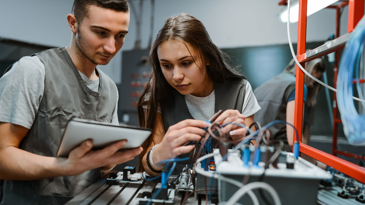Two junior engineers working with a tablet and a wiring system