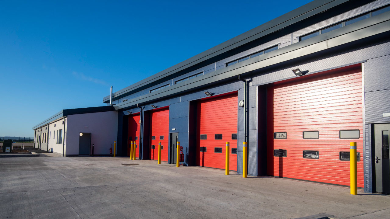 A modern industrial building featuring red garage doors and a sleek design, with clear blue skies overhead