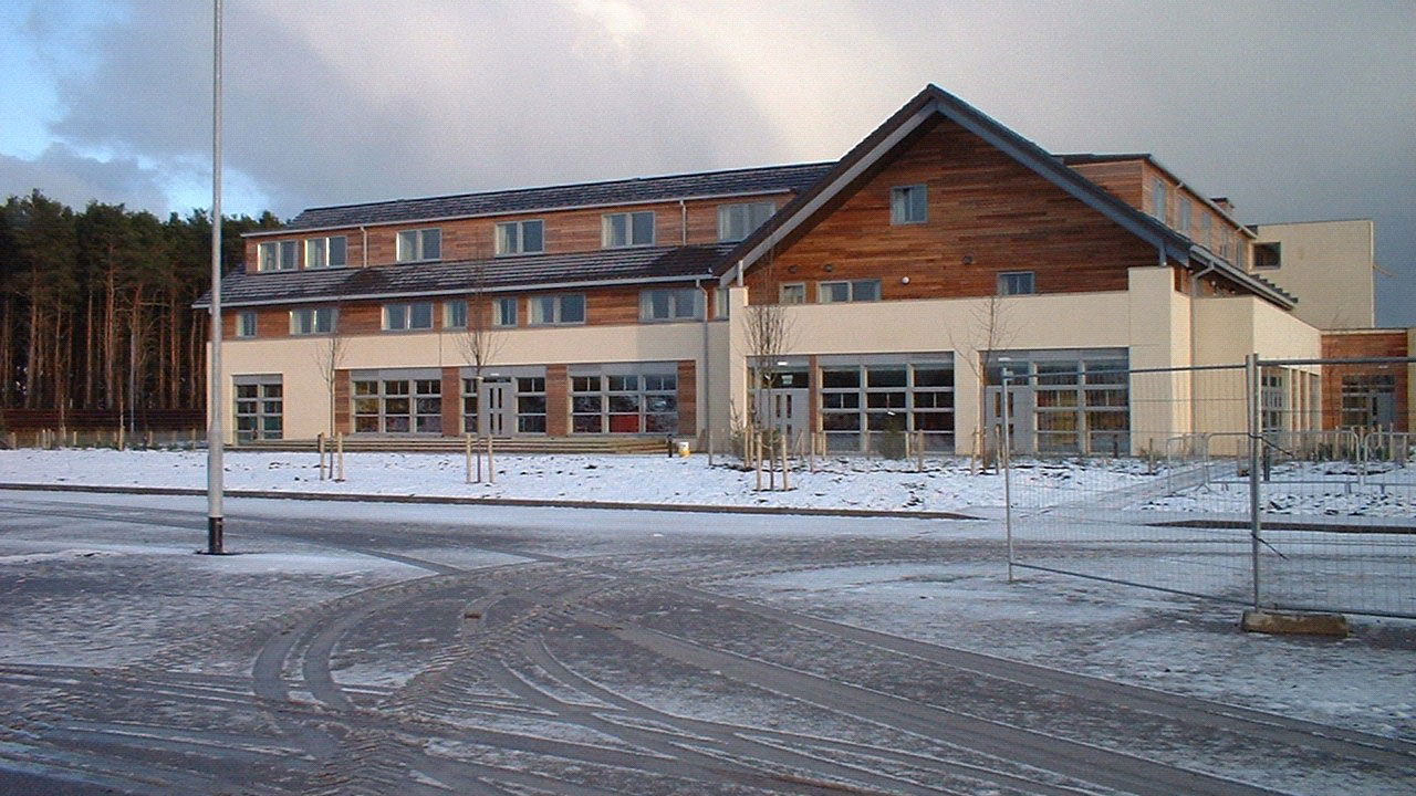 A modern building with a wooden facade, surrounded by snow and trees in the background
