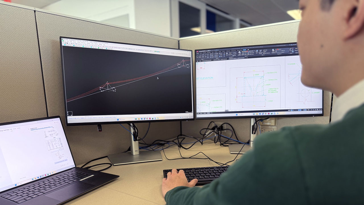 Engineer working at a desk with dual monitors displaying transmission line profiles and technical drawings for power transmission and distribution design
