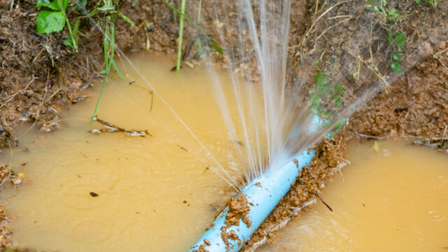 A close up of a leaking water pipe surrounded by flooding