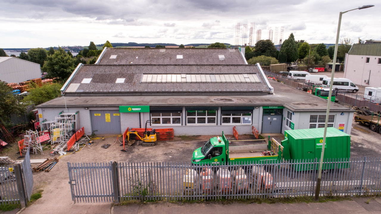 Aerial view of a commercial building with a green truck parked outside, surrounded by construction materials