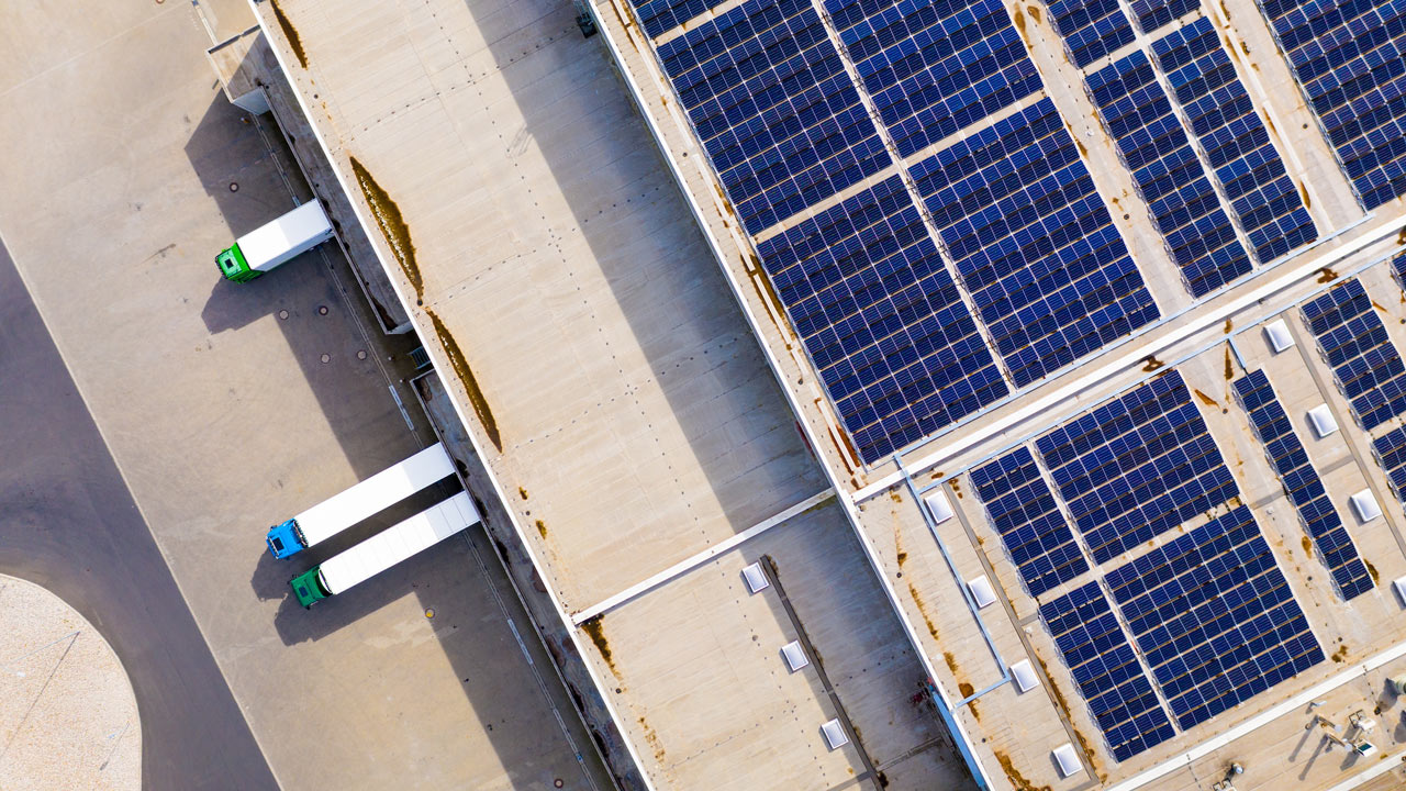 Aerial view of a logistics warehouse roof fitted with solar panels and delivery trucks at loading bays