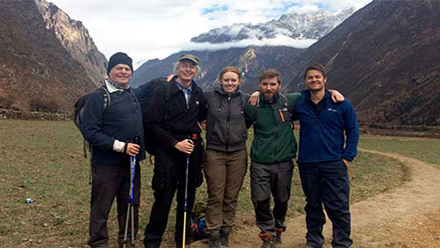A group of five hikers stands together on a grassy path in a mountainous landscape