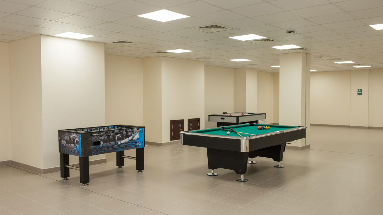 An indoor recreational area featuring a foosball table, a pool table, and an ice hockey table in a spacious room