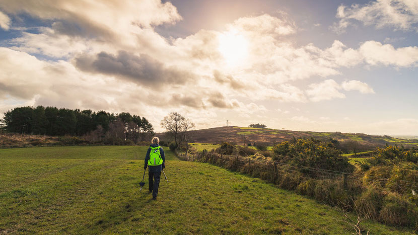 Worker in high visibility jacket walking across a field with a view towards a rural landscape