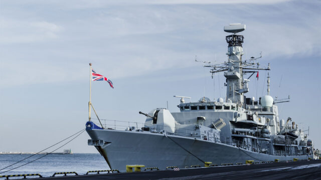 Military ship moored at the dockside with a view of the sea behind
