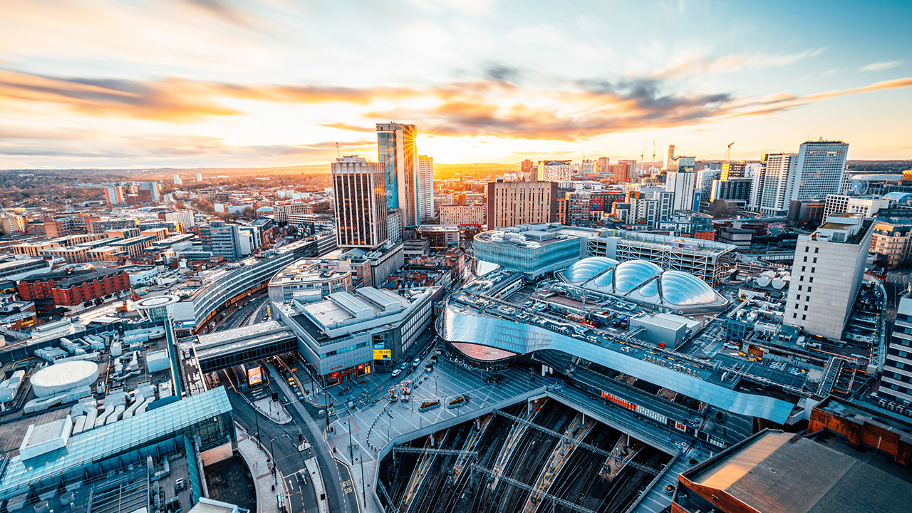 Aerial view of modern city skyline over a central station with curved-glass architectural buildings at sunset