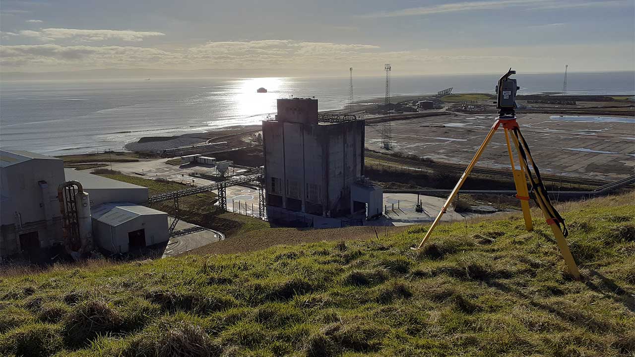 Wide lens view of the Aberthaw Power Station and geospatial surveying equipment on top of a hill with the sea in the background