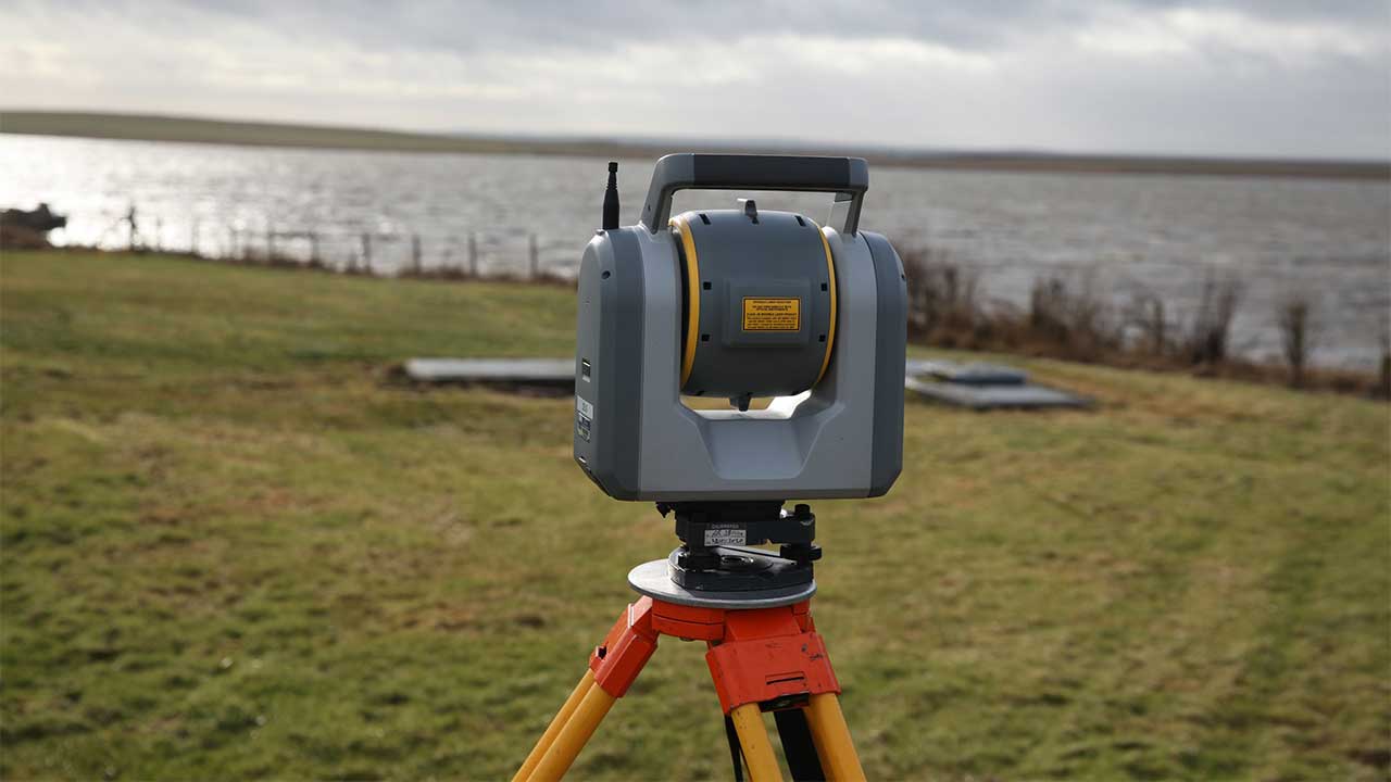 Surveying equipment being used in a field with a body of water in the background
