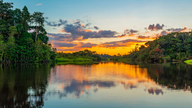 A lake reflecting a sunset and clouds surrounded by a tropical landscape