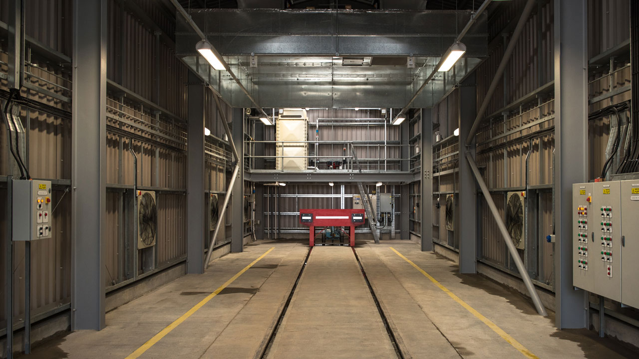 Interior view of a maintenance facility with railway tracks, control panels, and overhead equipment