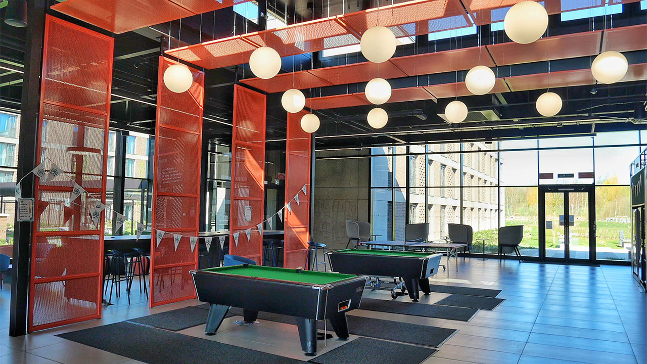 Photograph of an indoor community room with pool tables and lights