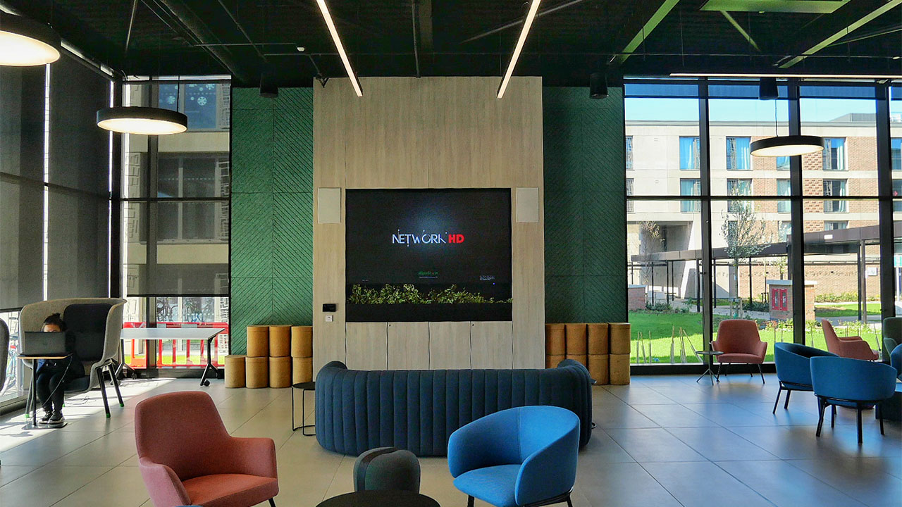 Photo of an indoor common area with couches, a television and tables for students
