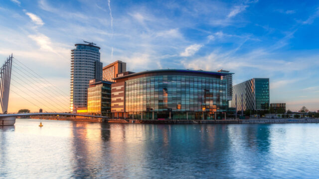 A modern waterfront building with bridge and high-rise in the background