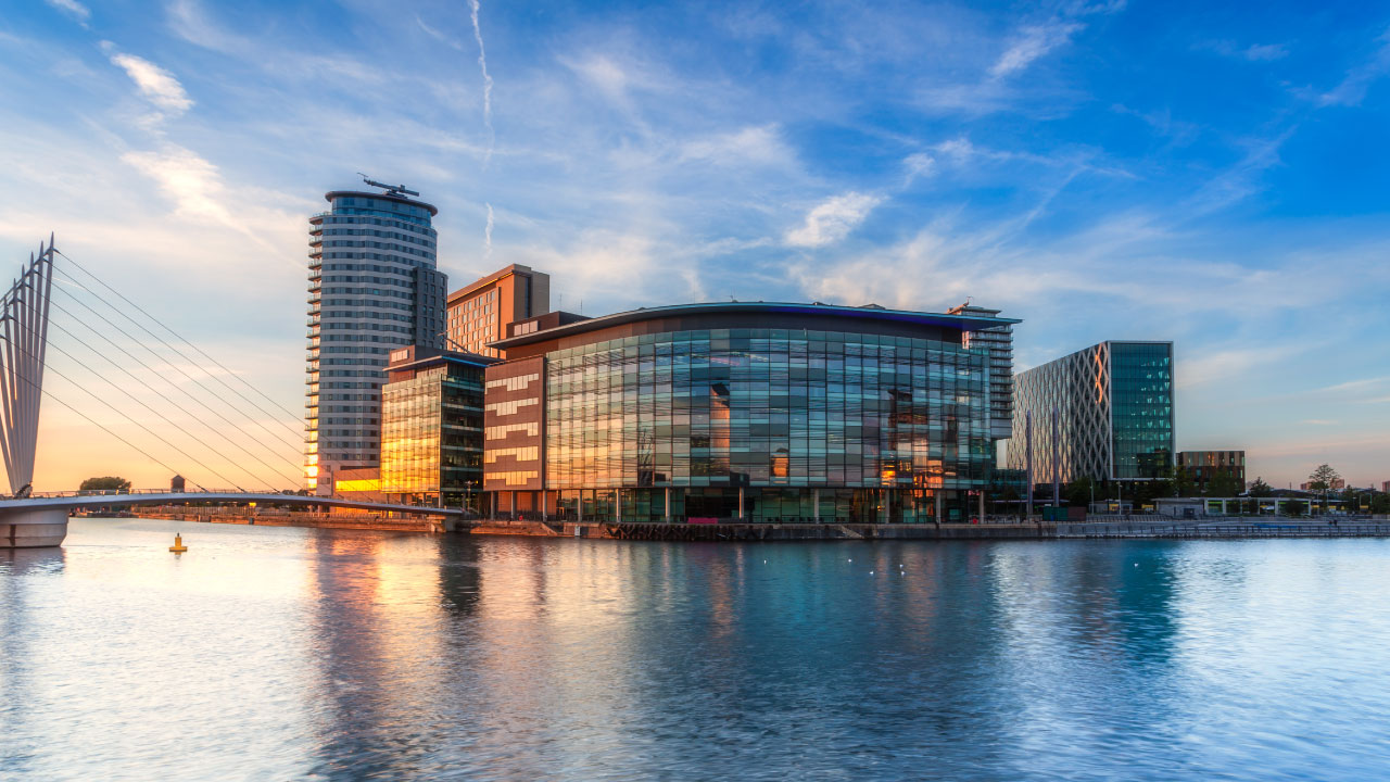 A modern waterfront building with bridge and high-rise in the background