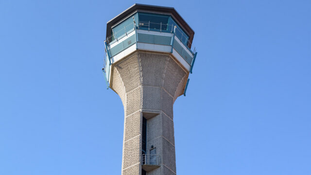 Control tower with octagonal glass cab atop textured concrete shaft against clear blue sky