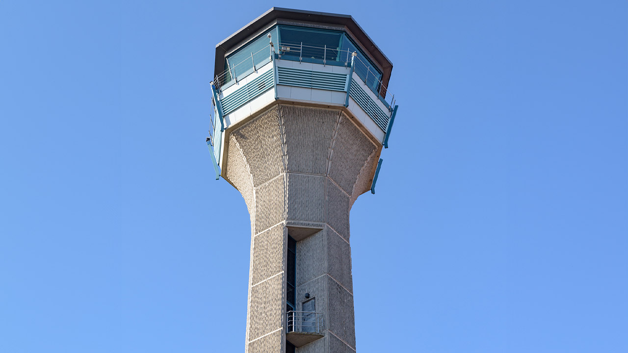 Control tower with octagonal glass cab atop textured concrete shaft against clear blue sky