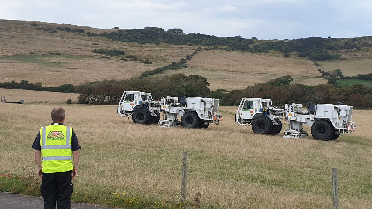 Two white survey trucks in rural countryside with a worker in a high-visibility jacket in the foreground