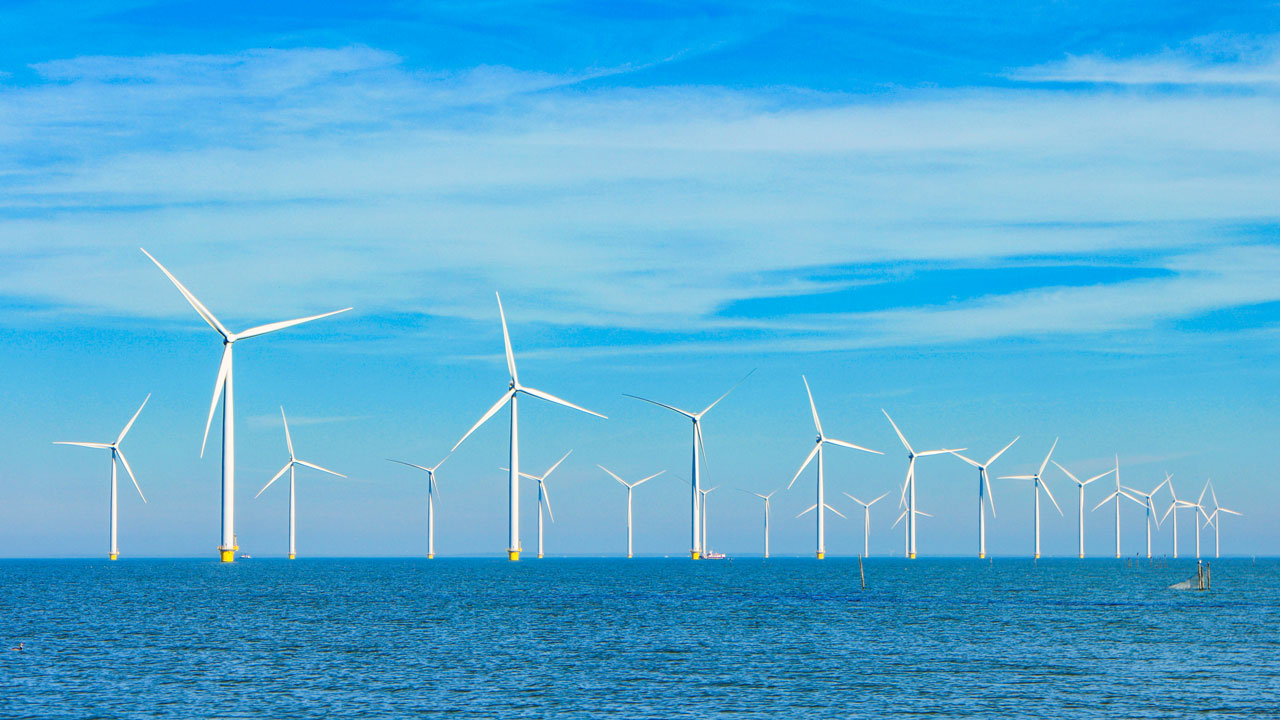Wind turbines on the horizon reflected in the sea, set against a bright blue sky