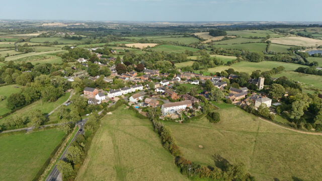 Aerial shot of rural village, residential houses and green fields