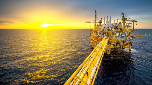 An oil drilling platform in the sea with a sun setting behind