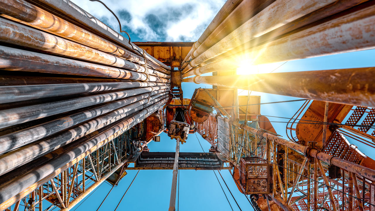 A view looking upwards at an oil drilling tower with the sun shining through the support struts