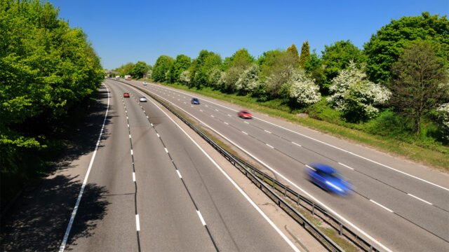 Aerial view of multilane road with cars driving on both carriageways and trees lining either side