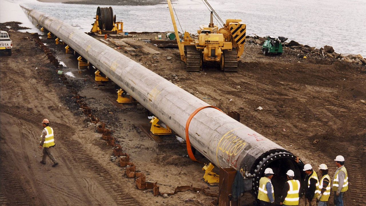 A photograph of a long, wide pipe surrounded by an engineering team