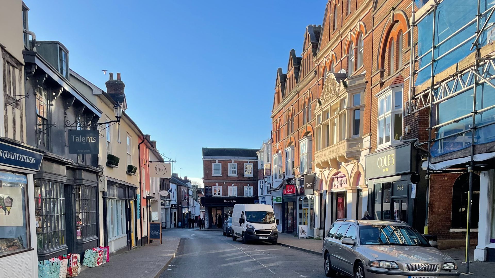 A lively street scene in a town center, featuring outdoor dining and pedestrians