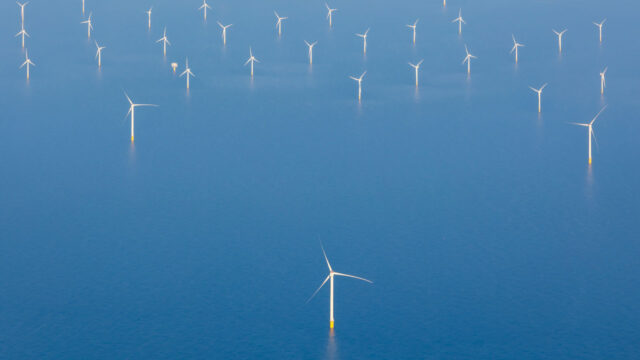 Aerial view of wind turbines in the distance against a blue sea