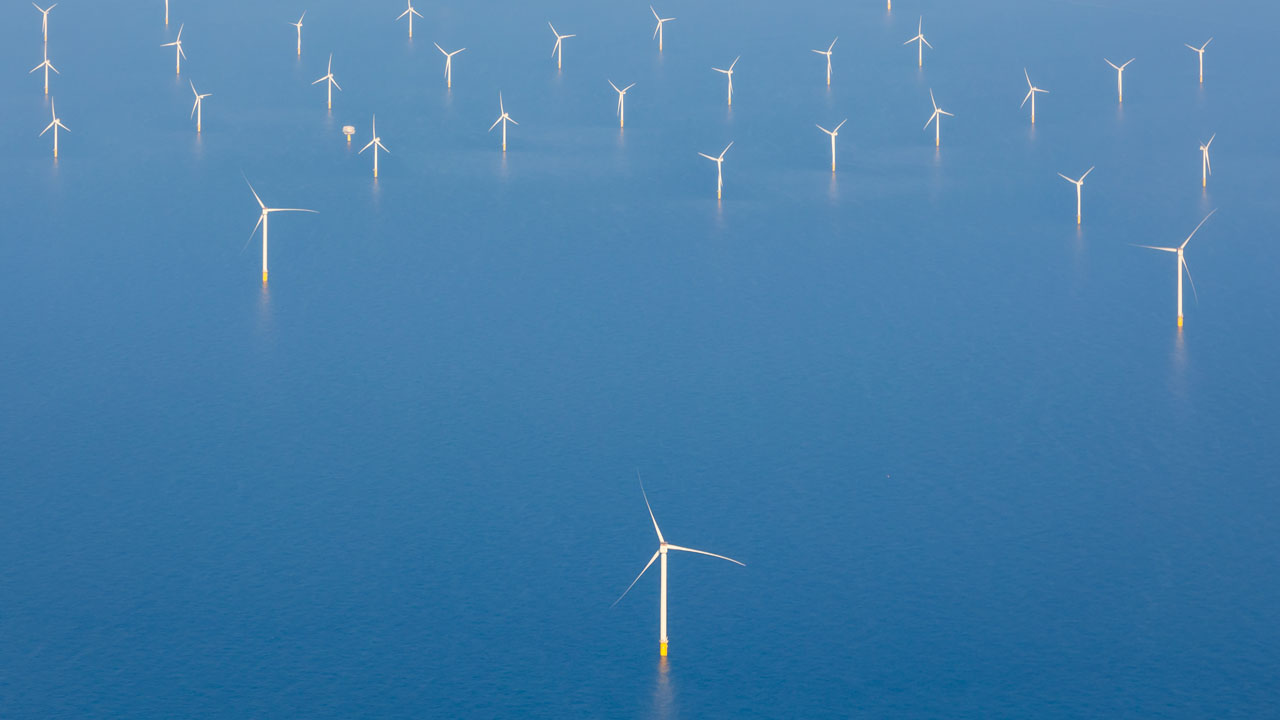 Aerial view of wind turbines in the distance against a blue sea