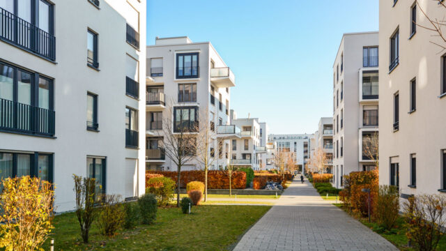 A large courtyard with planted flower beds and five storey residential buildings on either side with high-rise office buildings in the background
