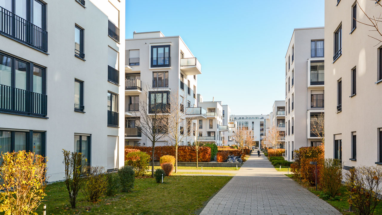 A large courtyard with planted flower beds and five storey residential buildings on either side with high-rise office buildings in the background