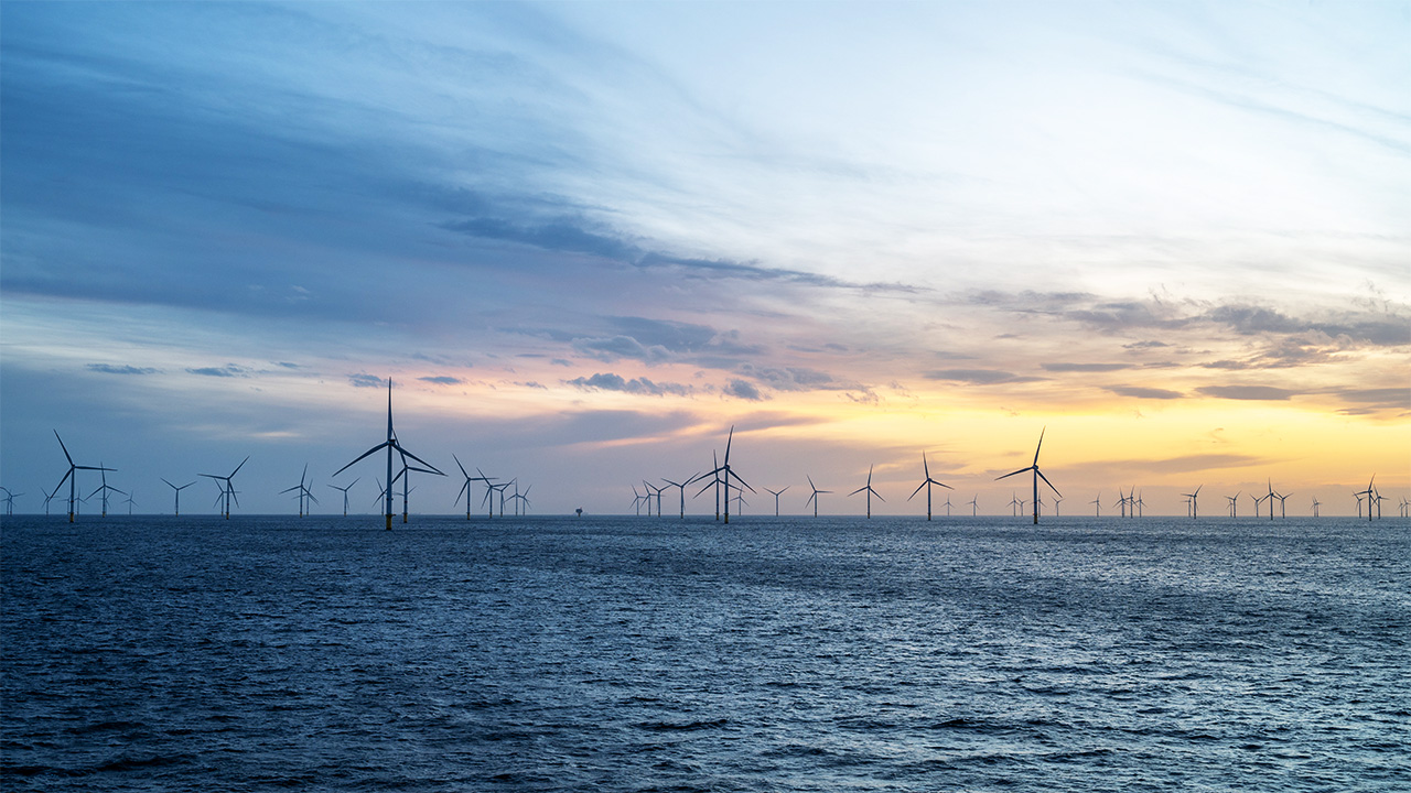 Offshore wind farm on the horizon against a sunset and windswept sky